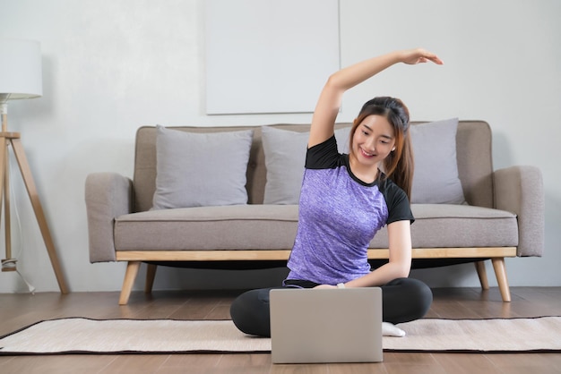Jovem asiática vendo vídeo de fitness no laptop e esticando o braço para relaxar depois do exercício