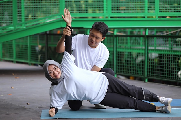 Jovem asiático ajudando sua esposa fazendo prancha no tapete de ioga no parque. Conceito de casal de estilo de vida saudável