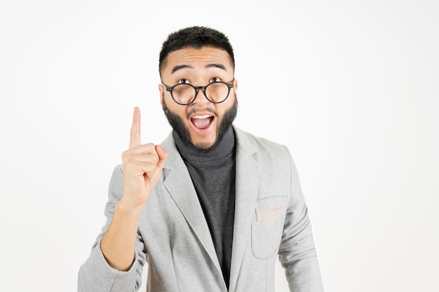 Jovem asiático bonito com barba vestindo jaqueta casual e óculos em fundo branco apontando com uma ideia de sucesso Bem-sucedido e feliz Número um