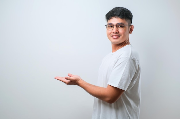 Jovem asiático bonito vestindo camisa casual com um grande sorriso no rosto apontando com o dedo da mão para o lado olhando para a câmera