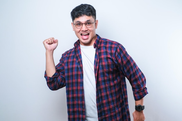 Jovem asiático bonito vestindo camisa casual e óculos em pé muito feliz e animado fazendo gesto de vencedor com os braços levantados sorrindo e gritando pelo sucesso Conceito de celebração