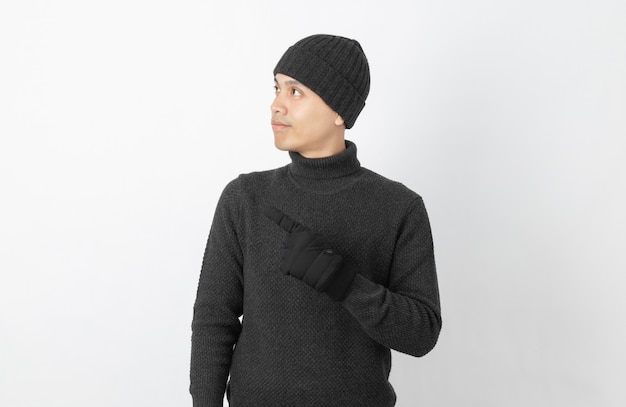 Jovem asiático bonito vestindo suéter cinza, luvas e gorro apontando para o lado com as mãos para apresentar um produto ou uma idéia