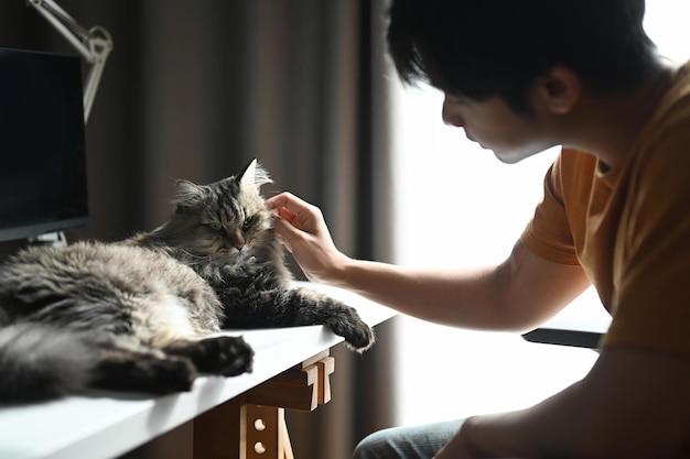 Jovem asiático brincando com seu gato fofo em casa