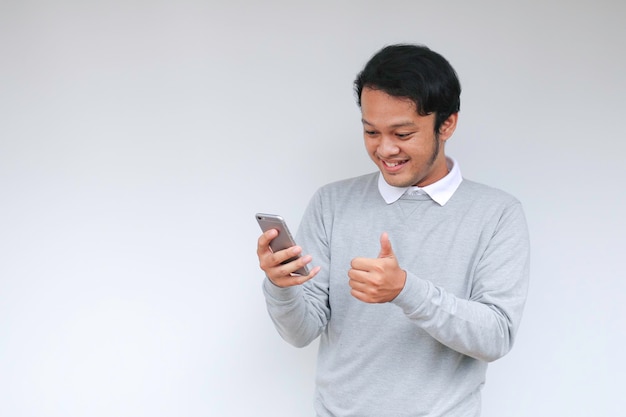 Jovem asiático chocado e feliz com o que vê no smartphone em fundo cinza isolado