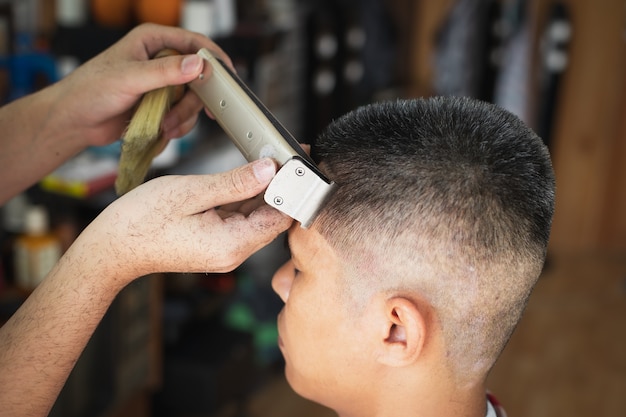 Foto jovem asiático com cabelos grisalhos, sendo cortado com uma máquina de tosquia elétrica por um barbeiro profissional na barbearia.