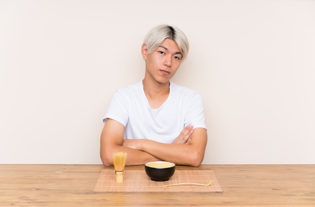 Jovem asiático com chá matcha em uma mesa, mantendo os braços cruzados