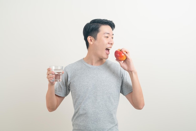 jovem asiático com copo de água e maçã na mão - conceito saudável
