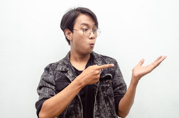 jovem asiático com óculos chocado alegremente apontando o dedo para copiar o espaço oferecendo algo de bens
