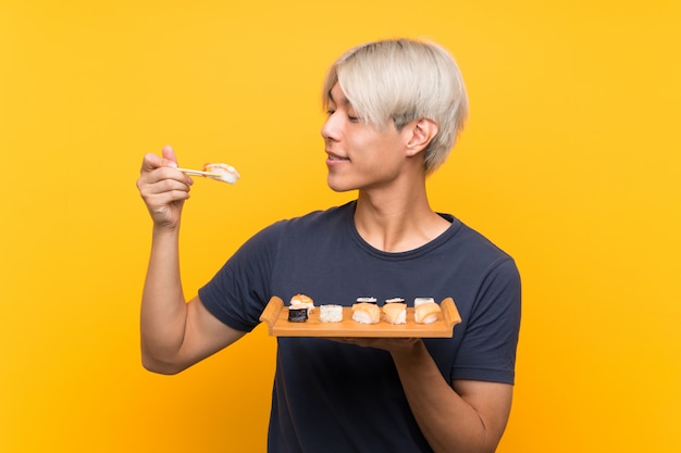 Jovem asiático com sushi sobre amarelo isolado