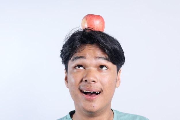 Jovem asiático com uma maçã na cabeça isolado em fundo branco