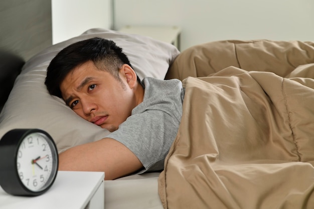 Jovem asiático deprimido deitado na cama não consegue dormir de insônia