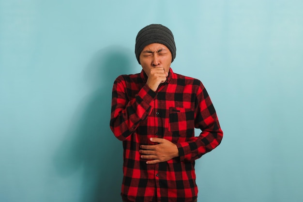 Jovem asiático doente está tossindo e espirrando sofrendo de uma gripe de tosse isolado em fundo azul
