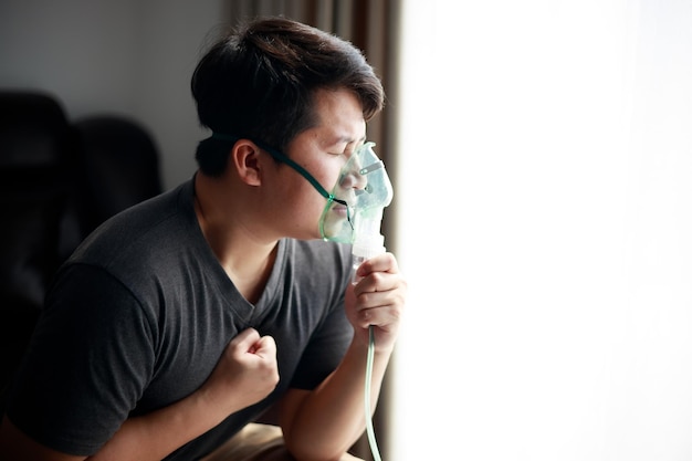Jovem asiático doente usando nebulizador para asma e doenças respiratórias em casa