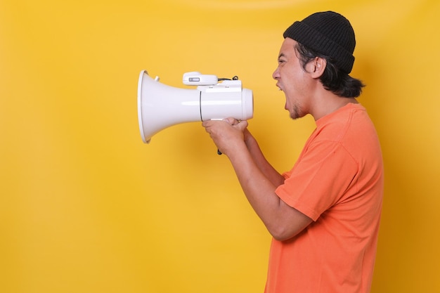 Jovem asiático em estilo casual isolado em fundo amarelo gritando através de um megafone Vista lateral