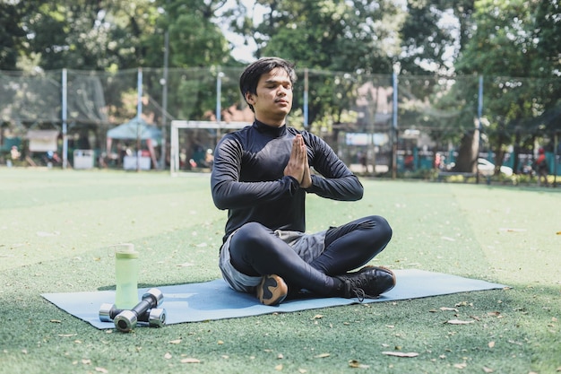 Jovem asiático em posição de ioga no parque de ginástica em tapete fazendo asana meditativa do lado de fora