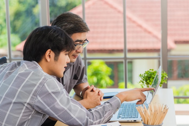 Jovem asiático ensinando pai sênior como usar um computador portátil moderno juntos na sala de estar em casa Filho ajudando pai a usar o laptop para aplicação web online