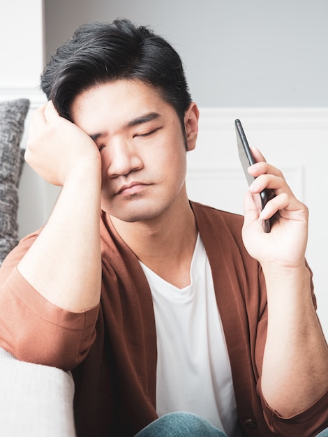 Jovem asiático esfregando os olhos cansados em seu smartphone.