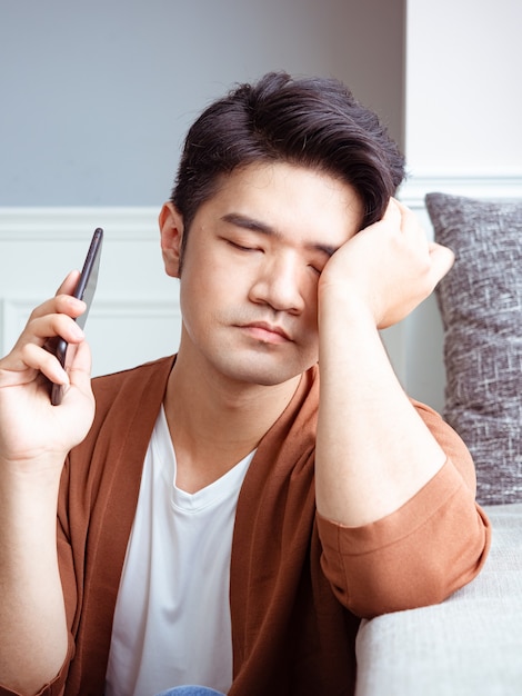 Jovem asiático esfregando os olhos cansados em seu smartphone.