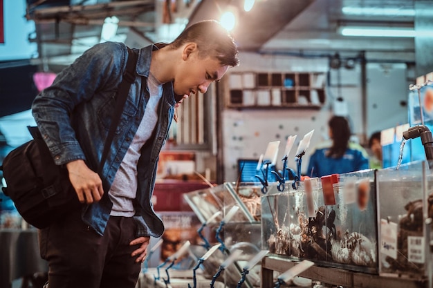 Jovem asiático está escolhendo frutos do mar no mercado local de chenise. ele compara preços e frutos do mar.