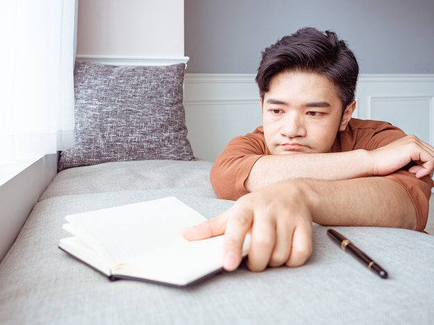 Jovem asiático fazendo uma pausa após ler um livro em casa