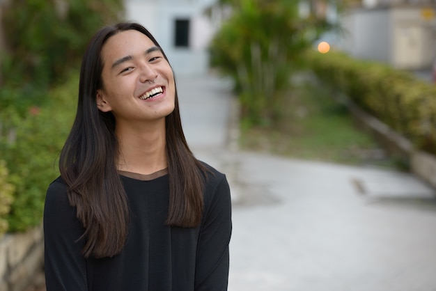 Jovem asiático feliz com cabelo comprido sorrindo para o parque