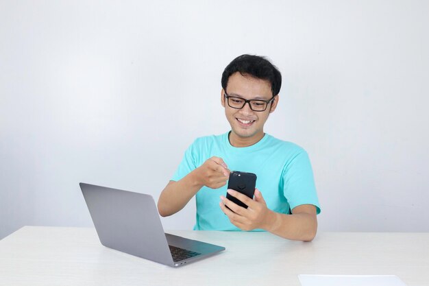 Jovem asiático feliz e sorri quando vê no telefone inteligente com laptop ao lado homem indonésio vestindo camisa azul