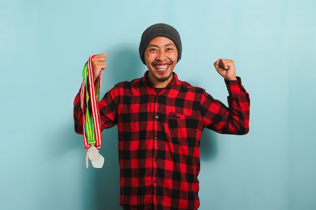 Jovem asiático feliz segura medalhas sorrindo e celebrando seu sucesso isolado em fundo azul