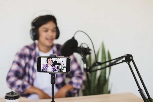 Foto jovem asiático gravando vídeo e gravando podcast usando smartphone e microfone no stand