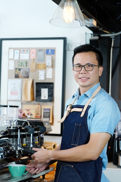Jovem asiático homem barista fazendo uma xícara de café no fundo do balcão do café