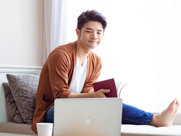 Jovem asiático lendo um livro enquanto relaxa em casa