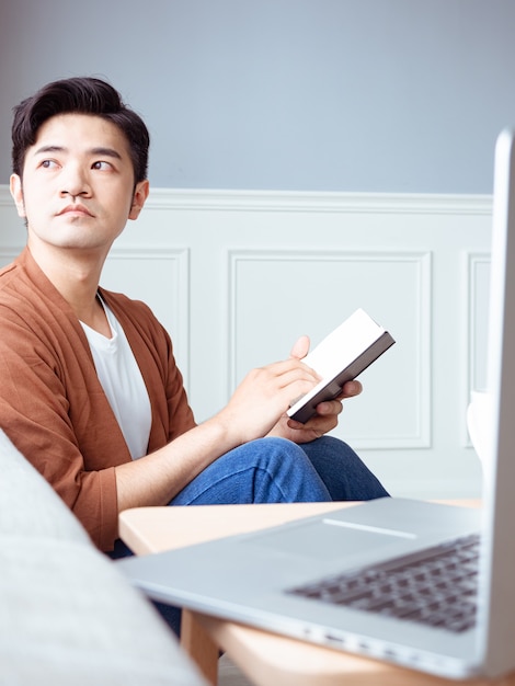 Jovem asiático lendo um livro enquanto relaxa em casa