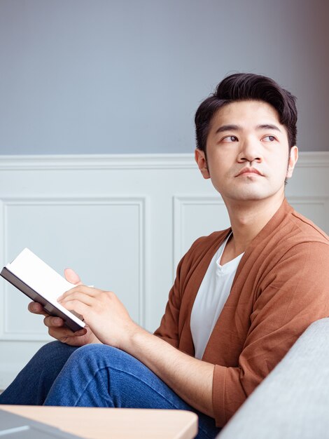 Jovem asiático lendo um livro enquanto relaxa em casa