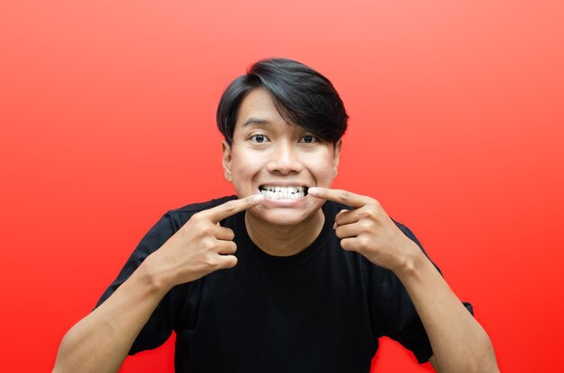 jovem asiático mostrando seus dentes tortos sobrepostos ou gigi gingsul isolado sobre fundo vermelho.