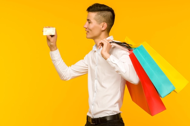 Jovem asiático mostrando sua sacola de compras e cartão de crédito em fundo amarelo