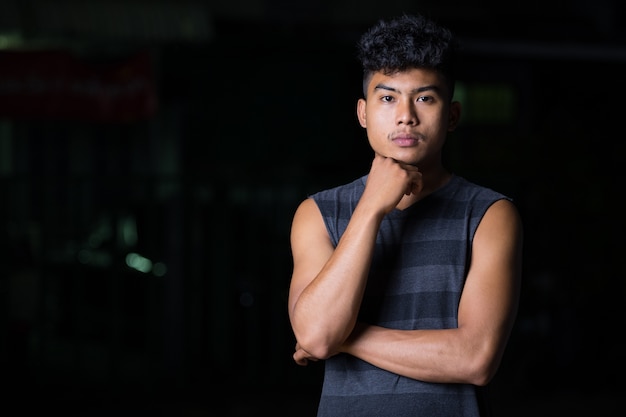 Jovem asiático pensando e olhando para a frente à noite ao ar livre