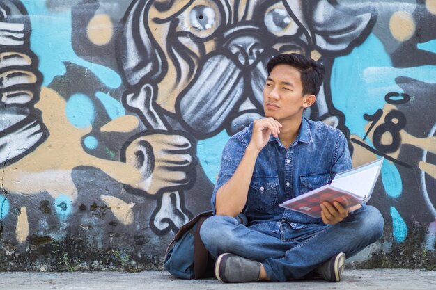 Jovem asiático pensando em ideias no parque usando um livro