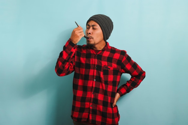 Jovem asiático saboreando comida com uma colher isolada em um fundo azul