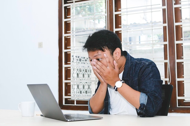 Jovem asiático se sentindo estressado e confuso quando trabalha laptop na mesa