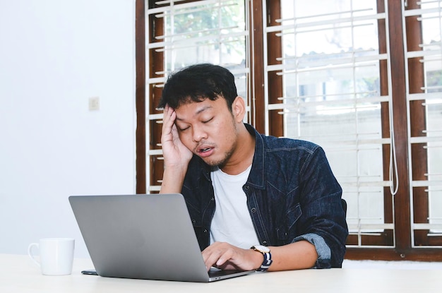 Jovem asiático se sentindo estressado e confuso quando trabalha laptop na mesa