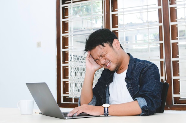 Jovem asiático se sentindo estressado e confuso quando trabalha laptop na mesa