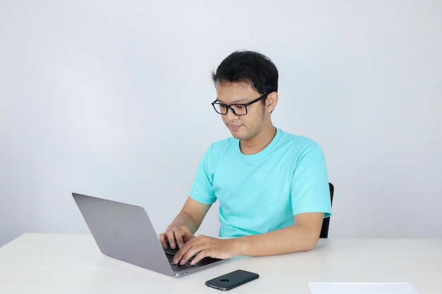 Jovem asiático se sentindo feliz e sorrindo quando trabalha laptop na mesa homem indonésio vestindo camisa azul