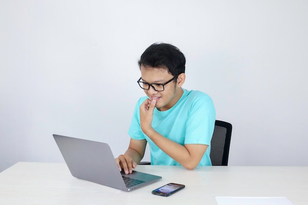 Jovem asiático se sentindo feliz e sorrindo quando trabalha laptop na mesa homem indonésio vestindo camisa azul