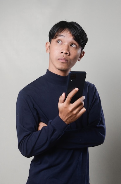 Jovem asiático segurando um telefone olhando de soslaio com expressão duvidosa e cética