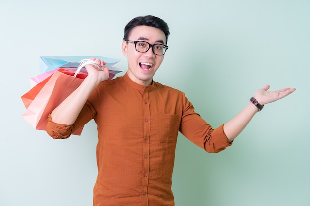 Jovem asiático segurando uma sacola de compras sobre fundo verde