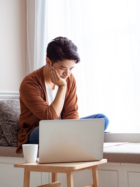 Jovem asiático sentado à mesa em frente ao computador portátil