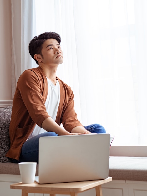 Jovem asiático sentado à mesa em frente ao computador portátil