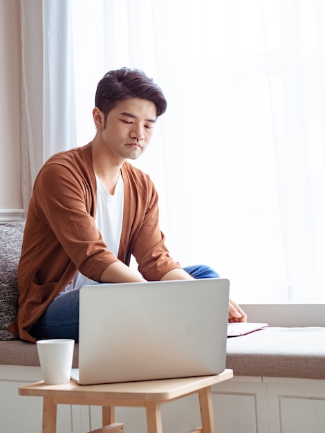 Jovem asiático sentado à mesa em frente ao computador portátil