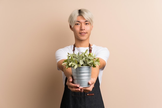 Jovem asiático sobre isolado tomando um vaso de flores