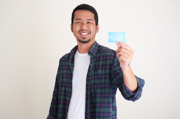 Jovem asiático sorrindo confiante ao mostrar seu cartão de crédito em branco