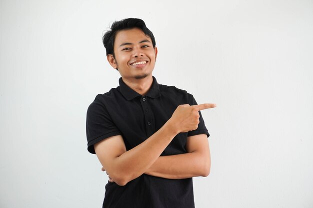 Foto jovem asiático sorrindo confiante com a mão apontando para o lado esquerdo vestindo camiseta de polo preta